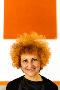 Woman with red curls in front of orange wall
