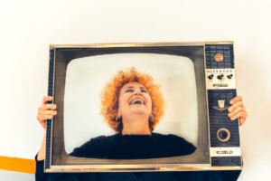 Red-haired woman smiling through TV set